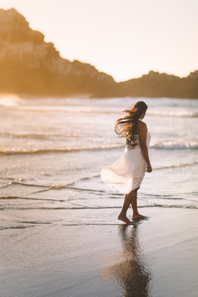 选择聚焦照片的女人站在海岸附近的岩层在金色的小时
